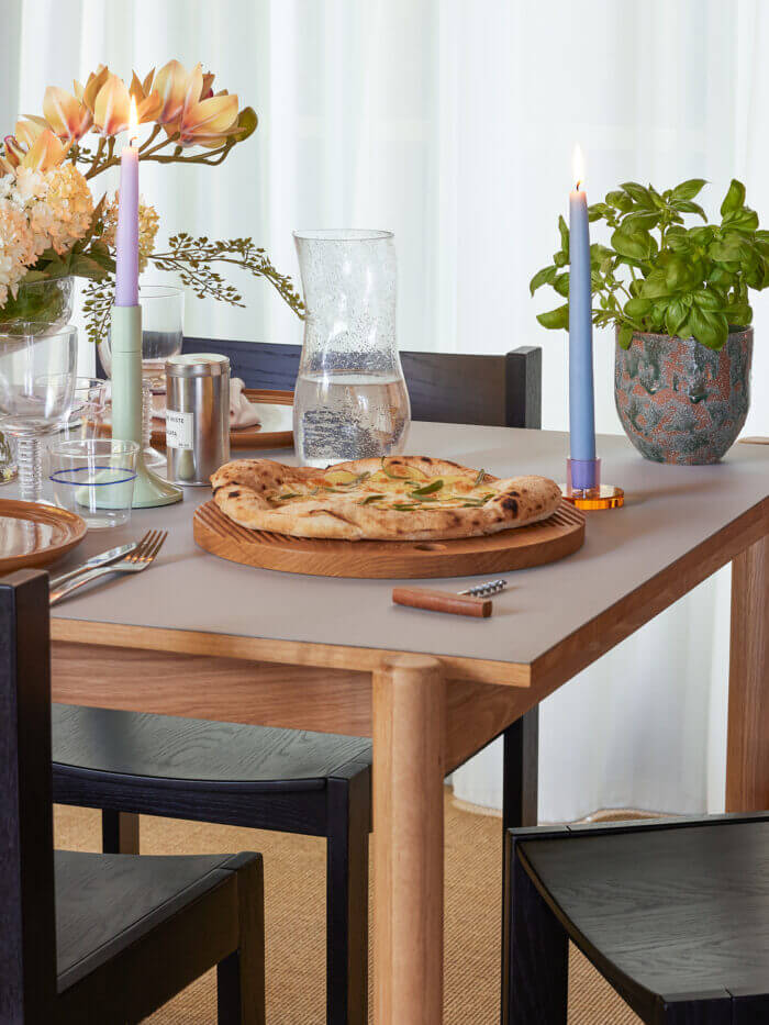 Skleněná karafa Bubble na prostřeném jídelním stole při večeři s pizzou, bazalkou a svíčkami.